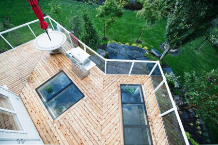 top-down angle of a wooden deck with glass skylight features overlooking a beautiful green backyard