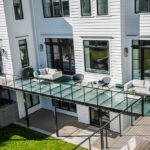 An image of a modern house with a large fully structural glass deck spanning across the back of the house overlooking the backyard.