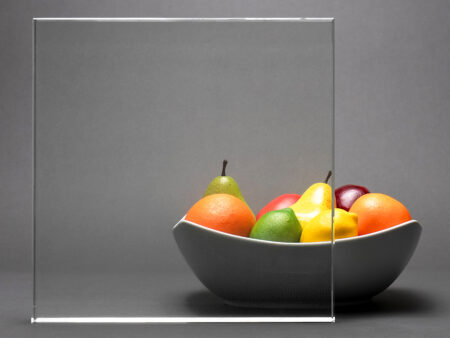 A square of nearly perfectly-transparent glass resting in front of a bowl of oranges, limes, and other fruits.