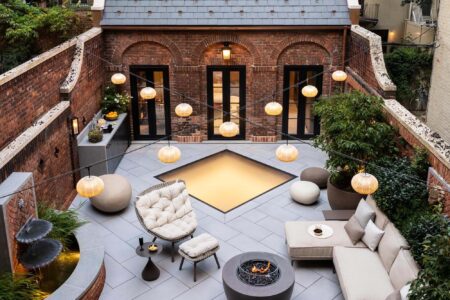 A cozy rooftop lounge featuring a square glass floor in the center, surrounded by outdoor seating, greenery, and decorative hanging lights.