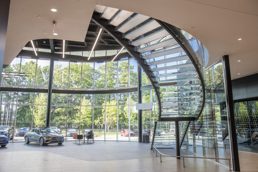 A stunning curved glass staircase inside the Mercedes-Benz showroom, featuring floor-to-ceiling windows and sleek, modern architecture.