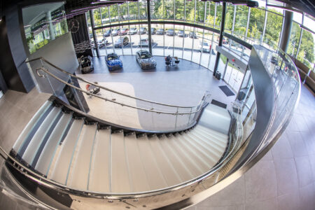 A top-down view of the Mercedes-Benz showroom glass staircase, elegantly curved with polished railings and glass steps, overlooking the showroom floor.