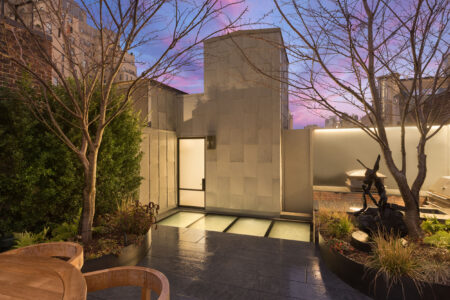 Modern rooftop garden with a sleek, illuminated glass floor integrated into the patio, surrounded by urban greenery and evening lighting.