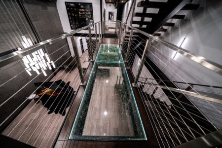 Glass walkway with polished railings and artistic lighting, creating a striking architectural feature in a contemporary home setting.