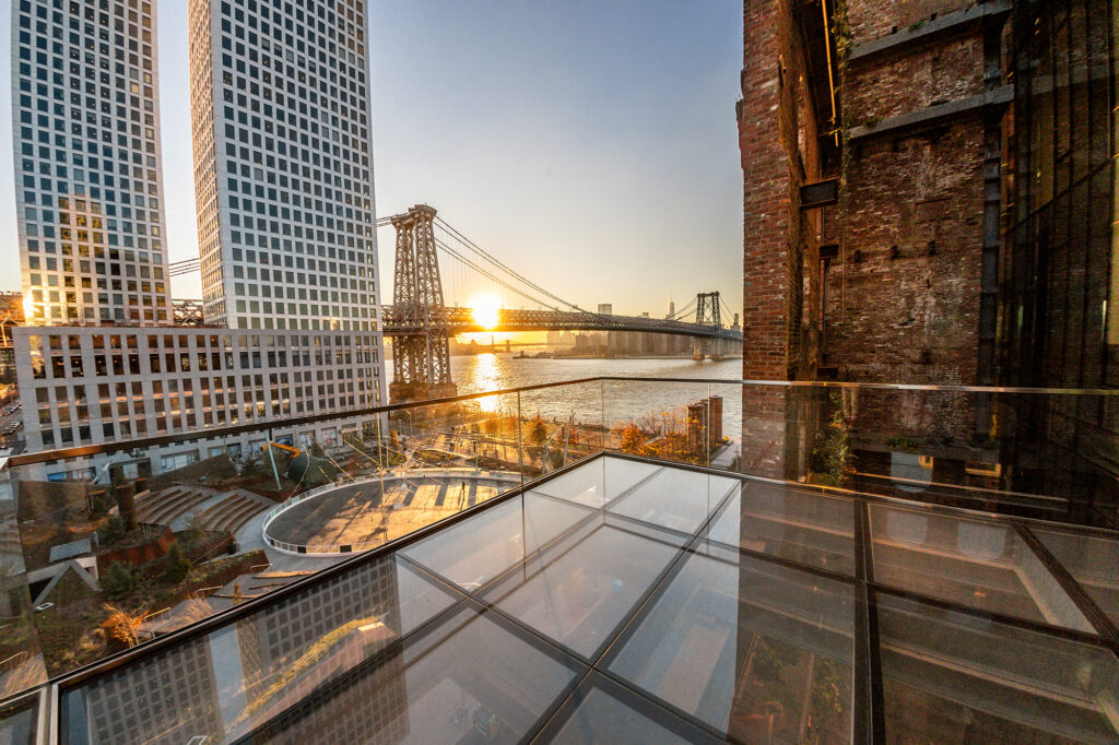 sunset view of the glass deck terrace with sunset reflections, highlighting the glass flooring and surrounding architectural design elements.
