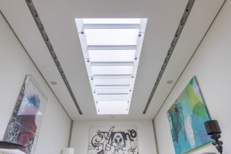 Minimalist room design featuring a rectangular glass skylight, framed by white walls, allowing light to flood the space artistically.