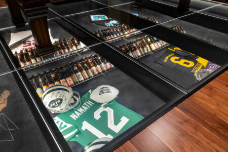 Close-up view of a glass floor displaying memorabilia, including vintage beer bottles and signed sports gear, showcasing a unique design element.