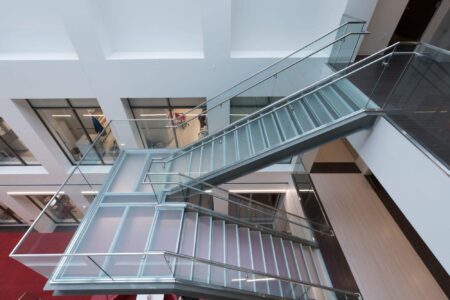 A sleek glass staircase with frosted steps and stainless steel railings, connecting multiple floors in a contemporary commercial building.