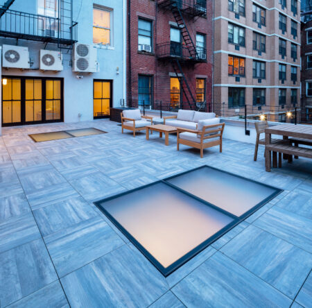 Stylish urban rooftop patio with multiple walkable glass skylights, outdoor seating, and wood-look tile flooring, perfect for city living.