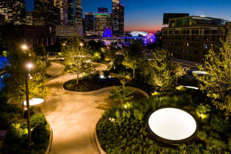 A vibrant urban park at night, illuminated by soft pathway lights, featuring circular walkable skylights labeled "Skylawn."