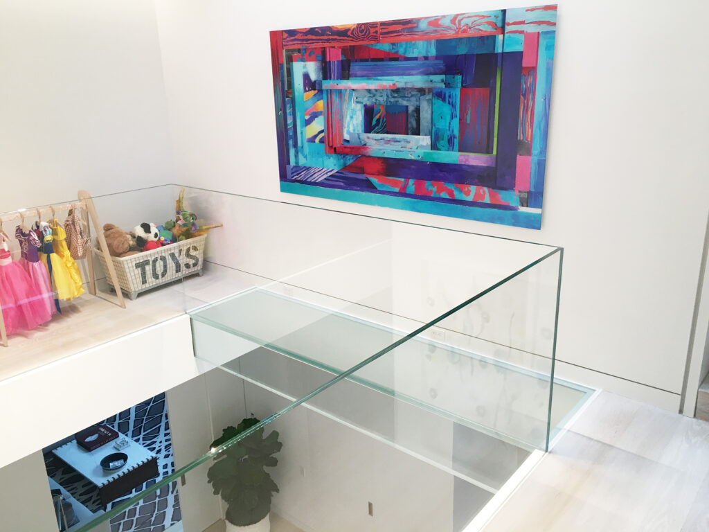 Residential play area with clear glass flooring and railing, featuring children’s dress-up clothes and colorful wall art.