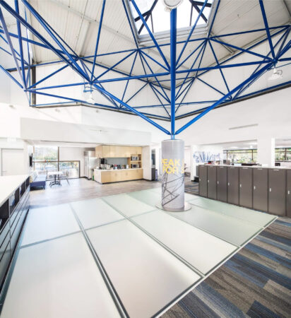 Sleek frosted glass floor panels integrated into a bright office space with blue steel roof trusses.