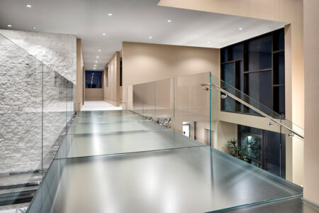 Frosted glass walkway in upscale home with stone accent wall, beige tones, and glass railing.