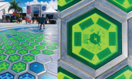 Colorful hexagonal solar tiles in green and blue patterns installed in a plaza outside a NASA facility.