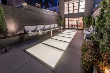 Outdoor patio with frosted walkable glass panels between modern seating areas and landscape lighting.