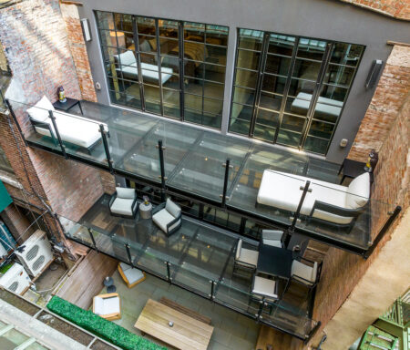 Two levels of glass balconies with clear railings extend from a loft-style residence, overlooking a private urban courtyard.