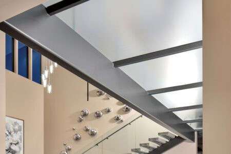 Frosted structural glass floor panels rest within a steel beam frame above a modern staircase and decorative accent wall.