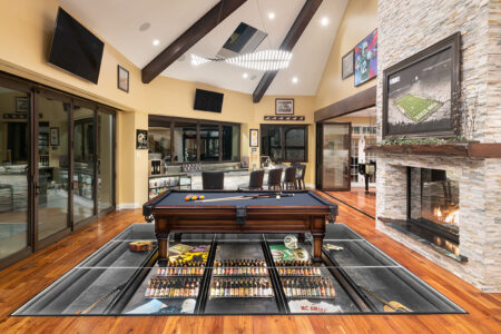 A pool table sits atop a glass floor showcasing a curated sports and beer collection in a luxurious entertainment room.