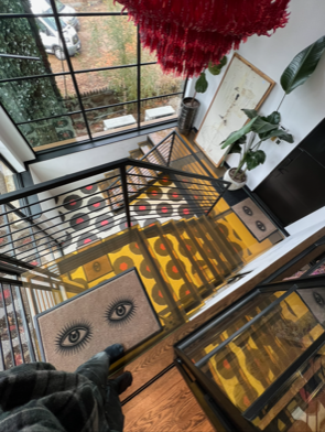 A colorful residential staircase with glass treads and unique patterned risers, enclosed by black railings in a sunlit foyer.