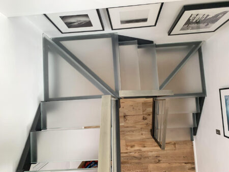 A contemporary staircase features frosted glass treads and black metal framing, positioned against white walls and decorated with black-and-white photography.