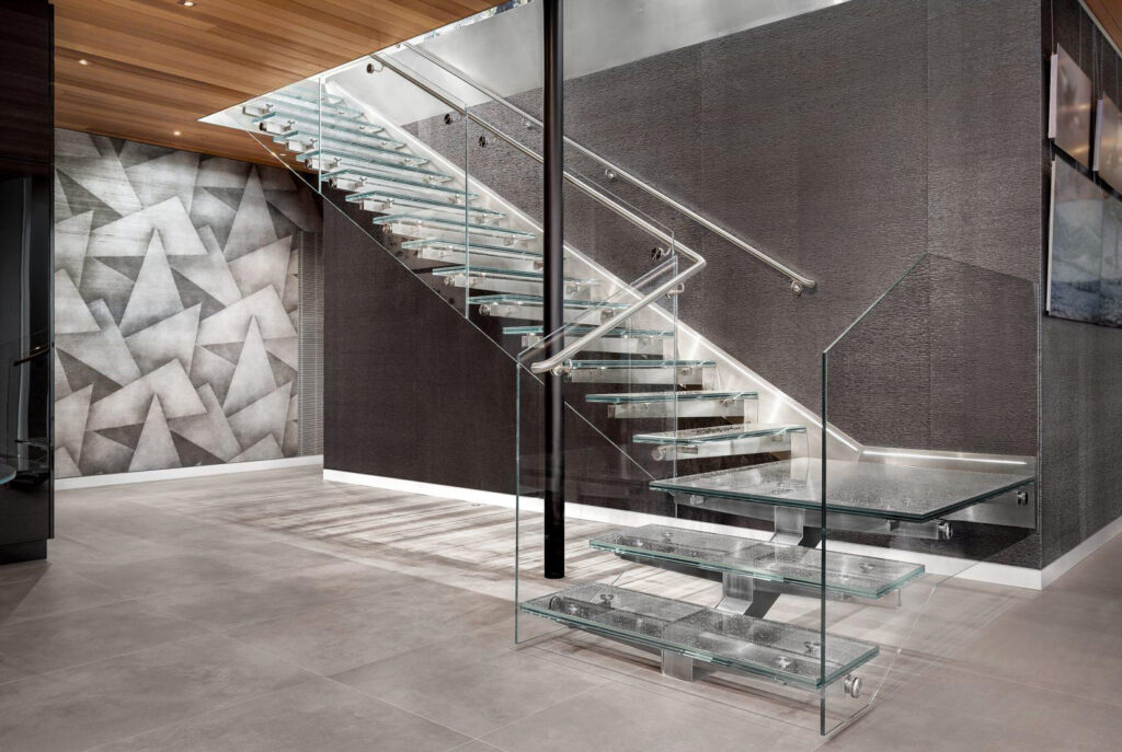A dramatic interior staircase showcases stacked clear glass treads, glass side panels, and stainless steel railings in a modern open-concept space.