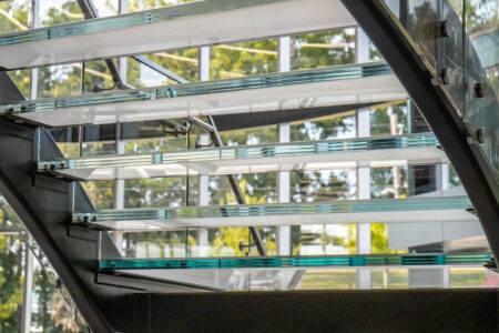 A glass staircase is illuminated by natural light, highlighting the clarity and layered edges of the laminated glass steps in a commercial setting.