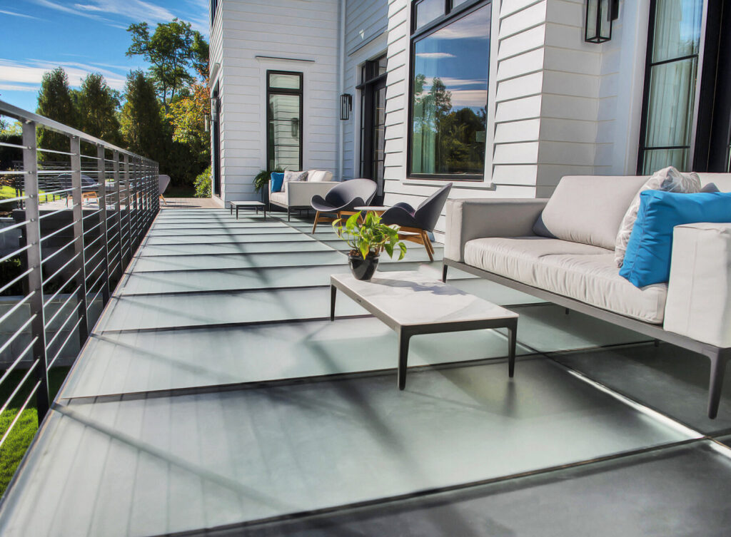 A modern home features a frosted glass patio floor with contemporary outdoor furniture and lush landscaping.