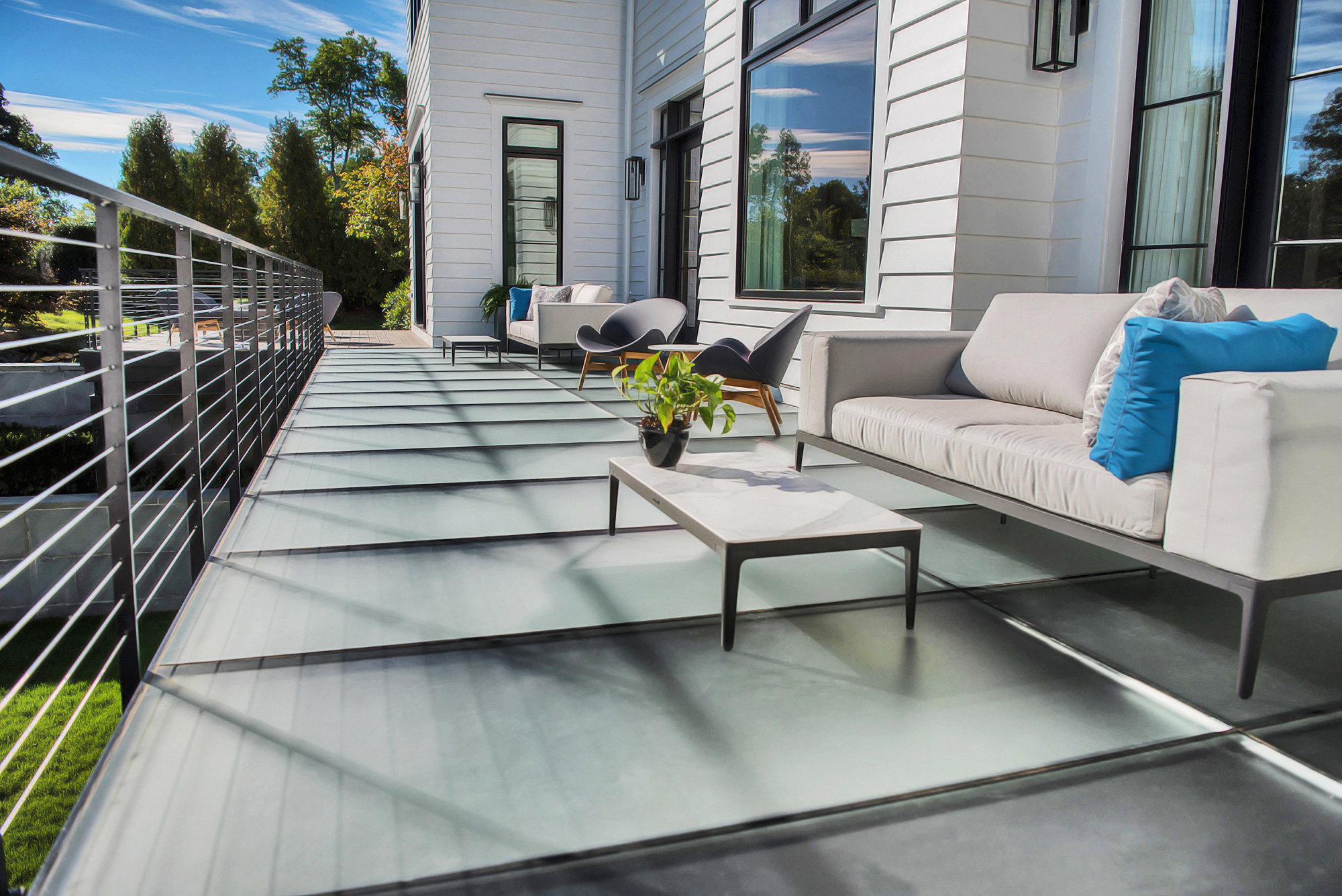 A modern home features a frosted glass patio floor with contemporary outdoor furniture and lush landscaping.