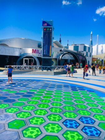 Visitors walk across a plaza featuring colorful hexagonal glass tiles with Vanceva Colored Interlayers at NASA’s Kennedy Space Center under a bright blue sky.