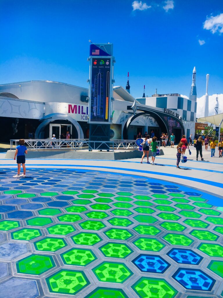 Visitors walk across a plaza featuring colorful hexagonal glass tiles with Vanceva Colored Interlayers at NASA’s Kennedy Space Center under a bright blue sky.