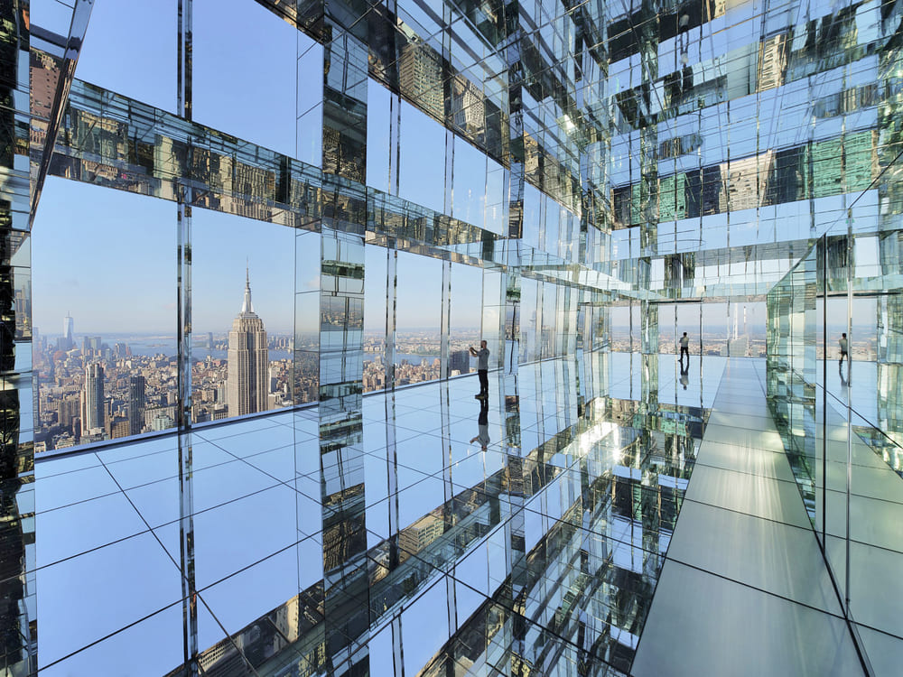 Glass observation deck with mirrored walls overlooking a skyline at sunset.
