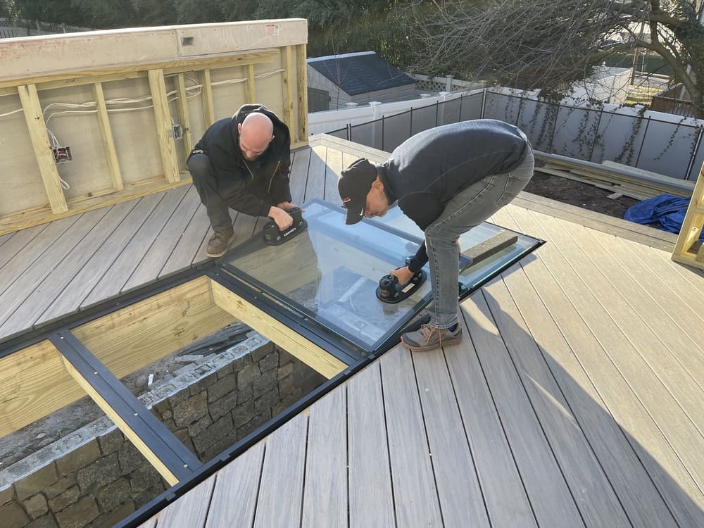 Two men are installing glass flooring on a residential building.