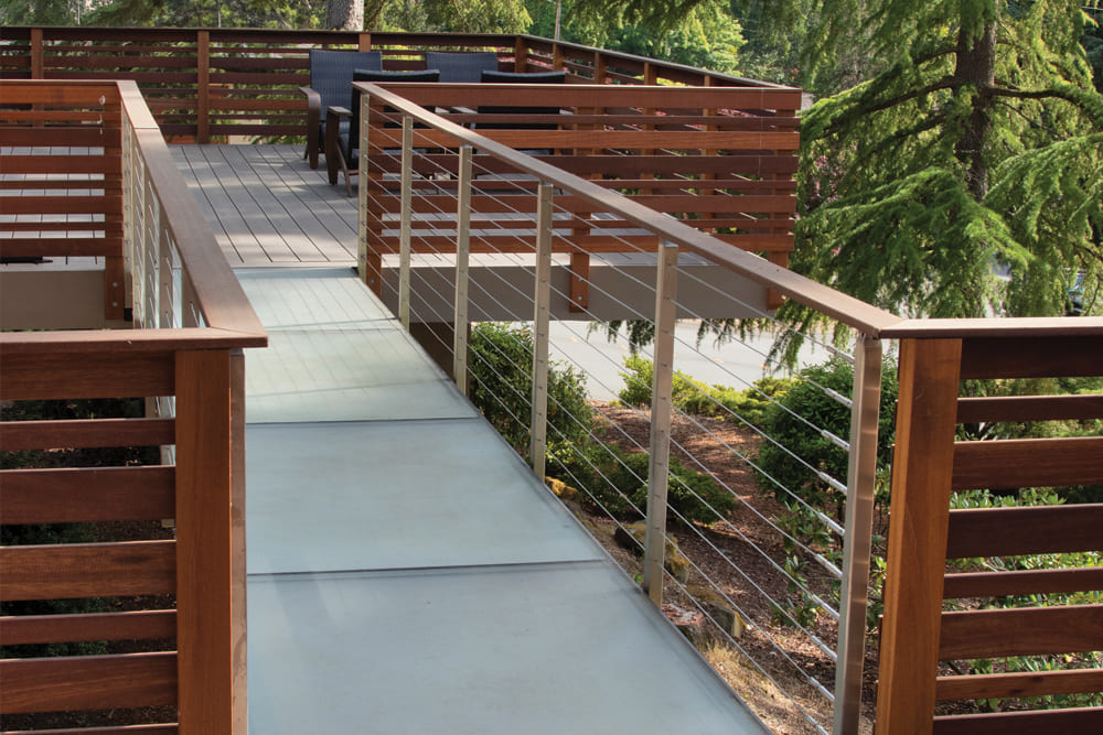 An outdoor pathway with wooden fencing and sleek cable railings surrounded by greenery.