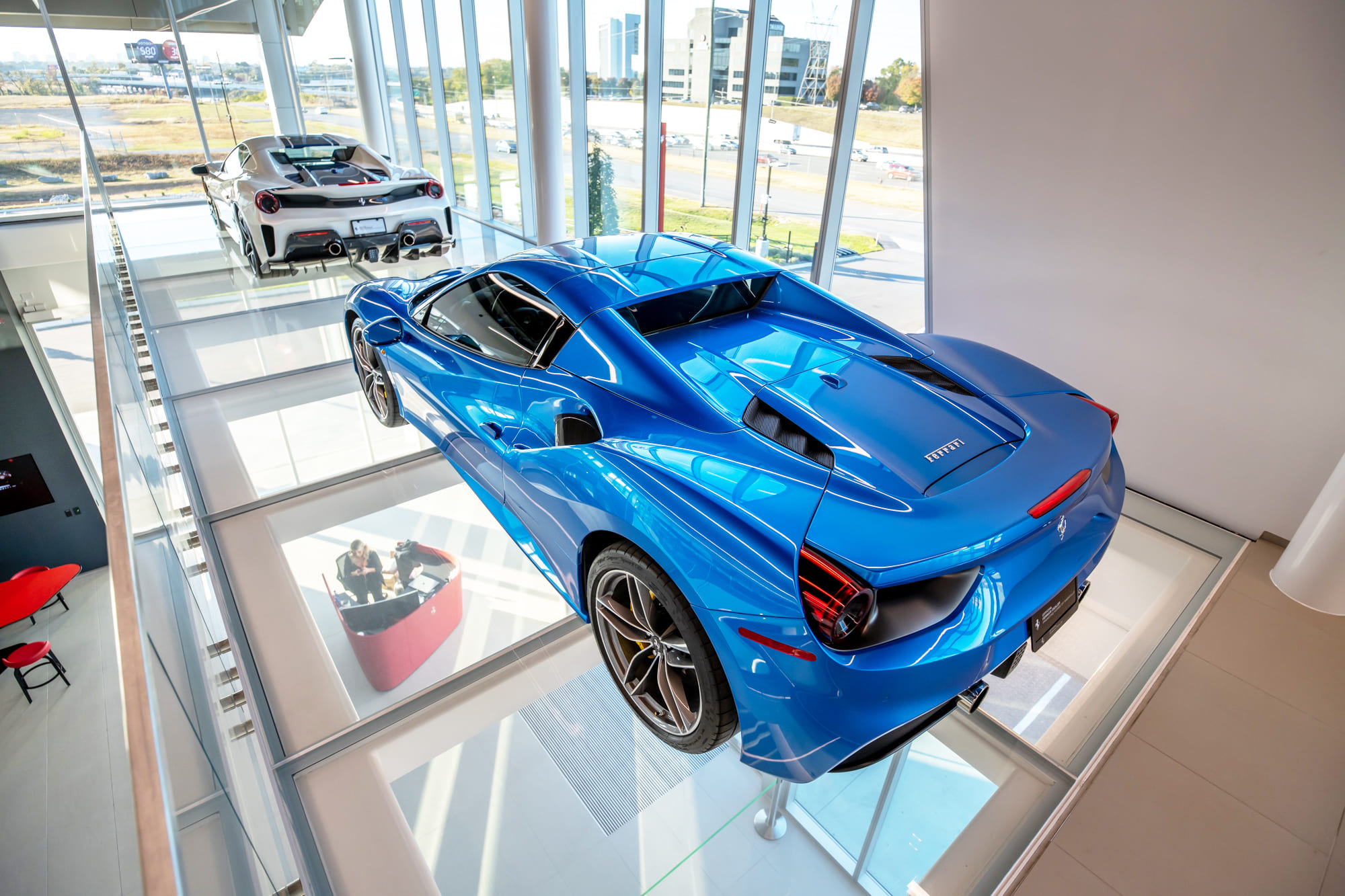 Two luxury cars in a showroom are placed over a glass floor panel.