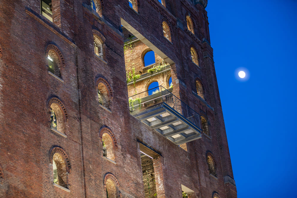 Glass balcony extension on a brick building illuminated at dusk, creating a dramatic architectural feature.