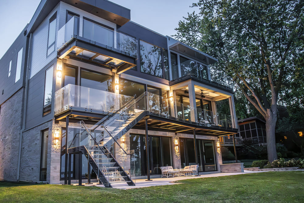 Large modern residence featuring illuminated glass balconies and tiered outdoor spaces at night.