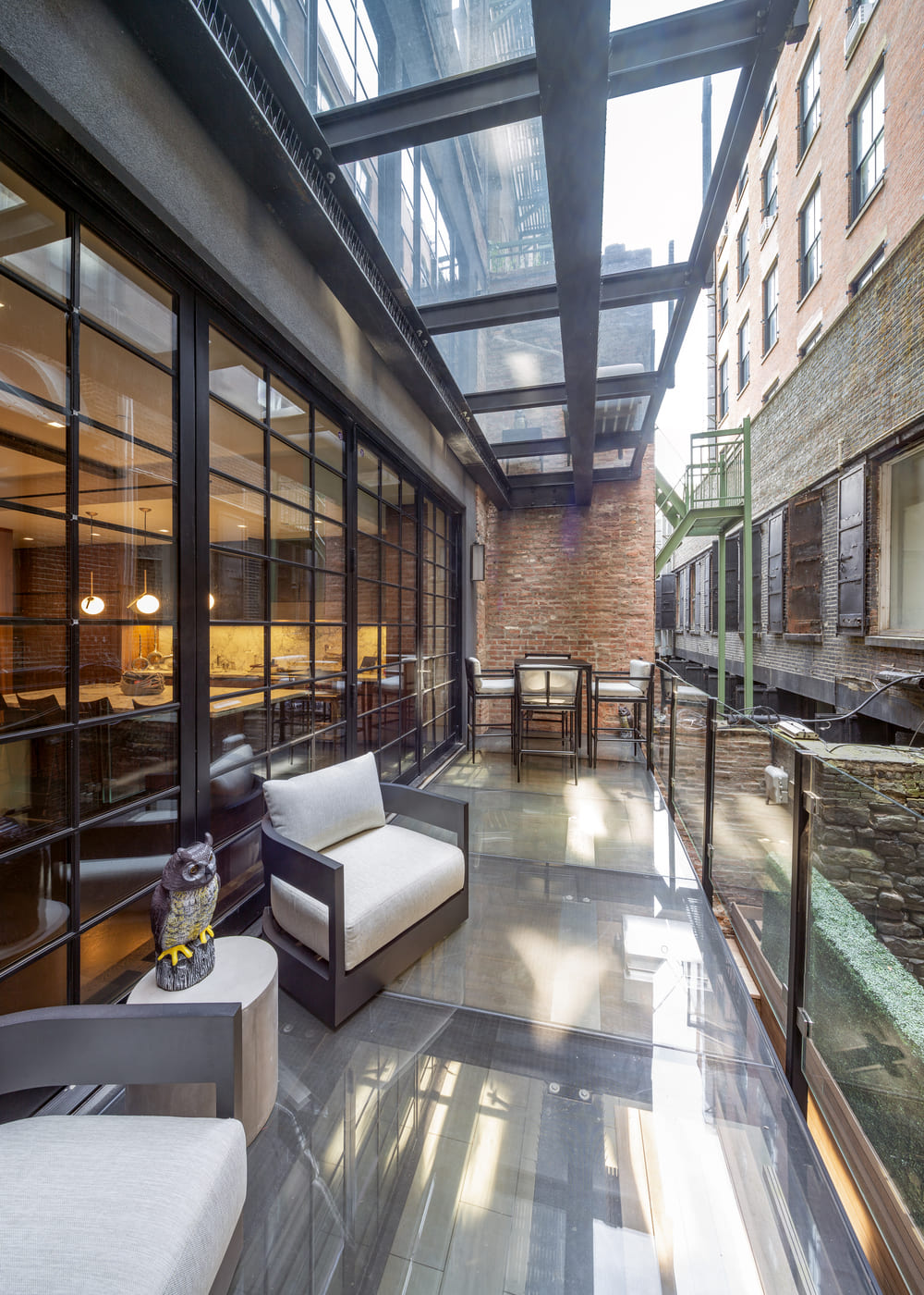 Luxury outdoor seating area with clear glass floor panels and transparent railing integrated into a multi-story building facade.