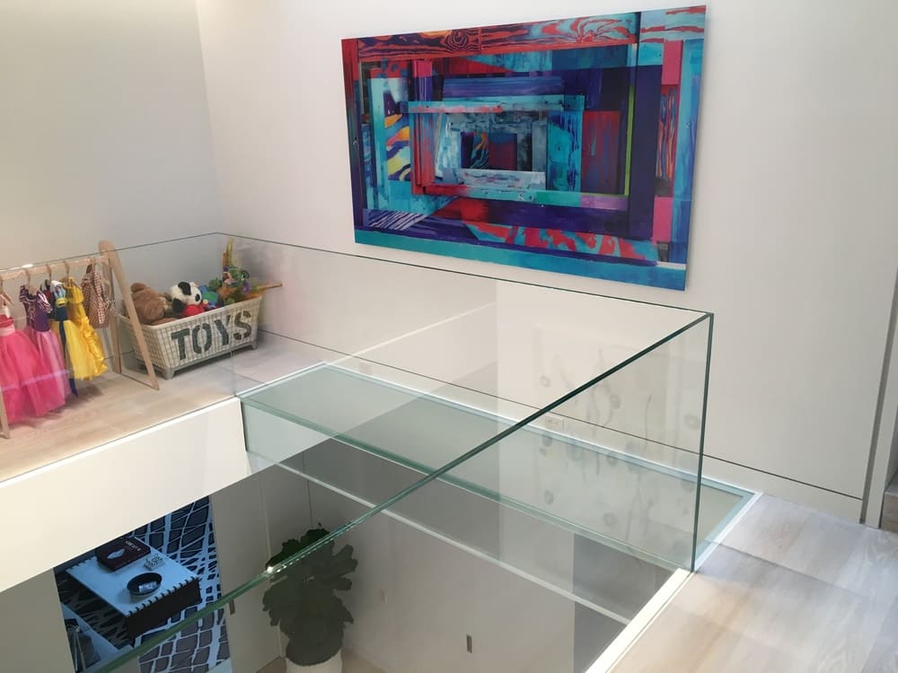 Modern indoor balcony with clear glass railings and colorful wall art in a bright white room.