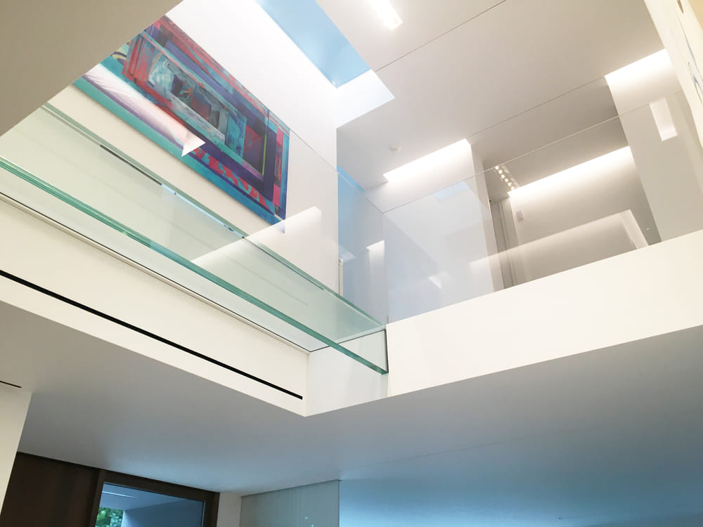 Interior of a contemporary home with large glass railings around an upper walkway under natural light.