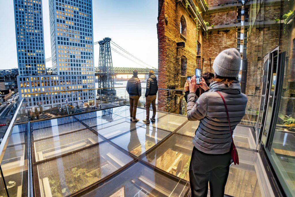 A glass-paneled view deck with a view of the city, the river, and a vintage wall.