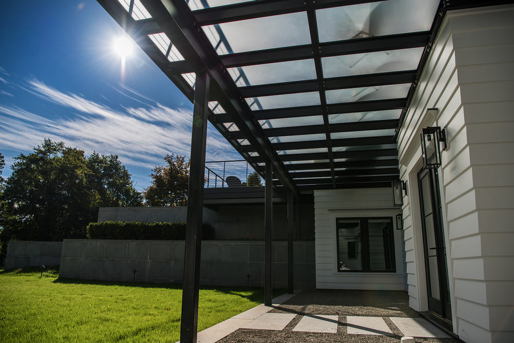 Glass patio roof system providing shade and weather protection over an outdoor residential space.