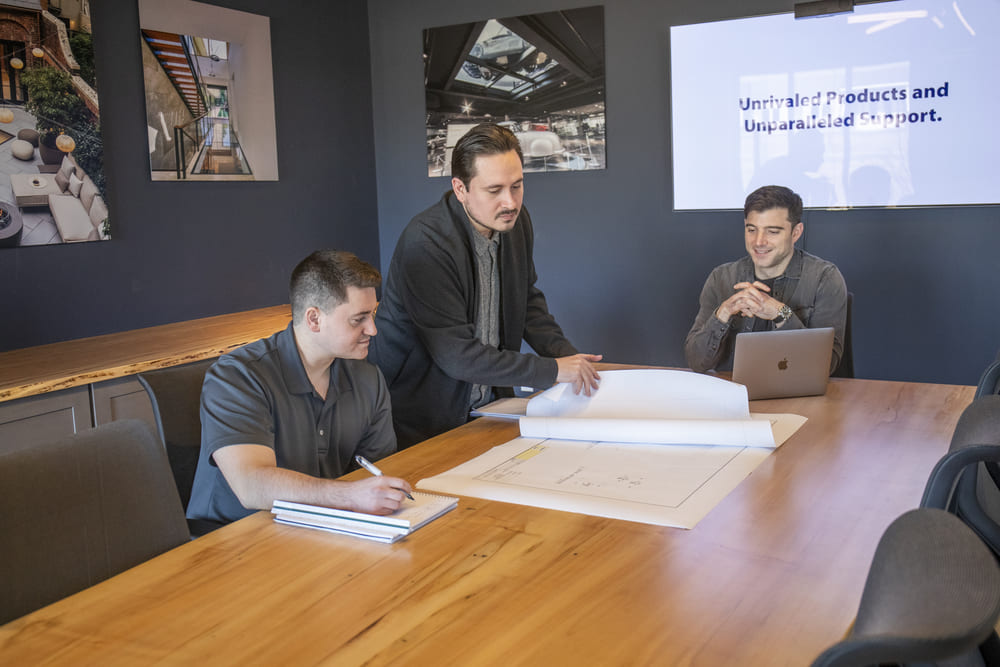 Three men are in a meeting room discussing a project.