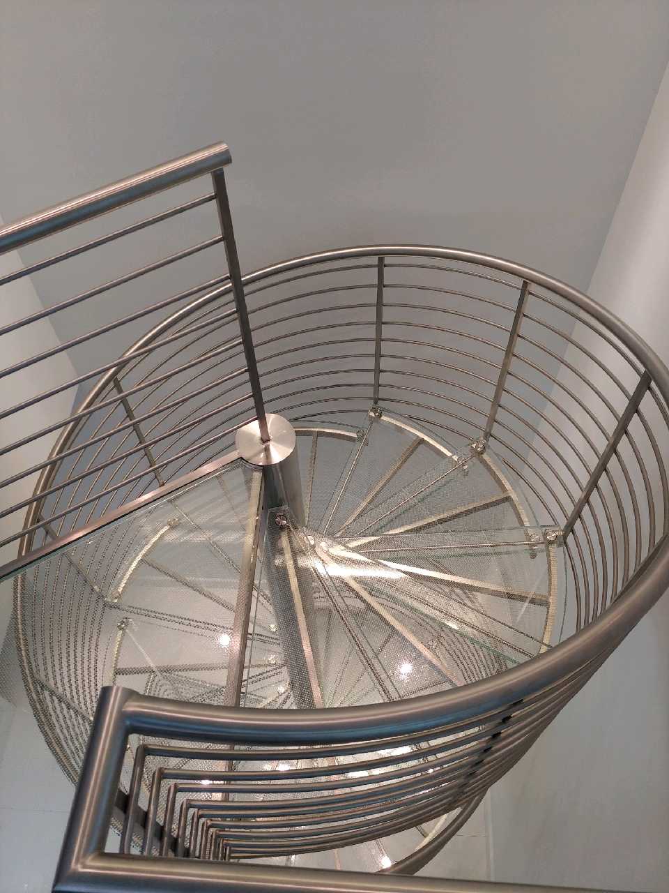 Spiral metal staircase with glass steps viewed from above.