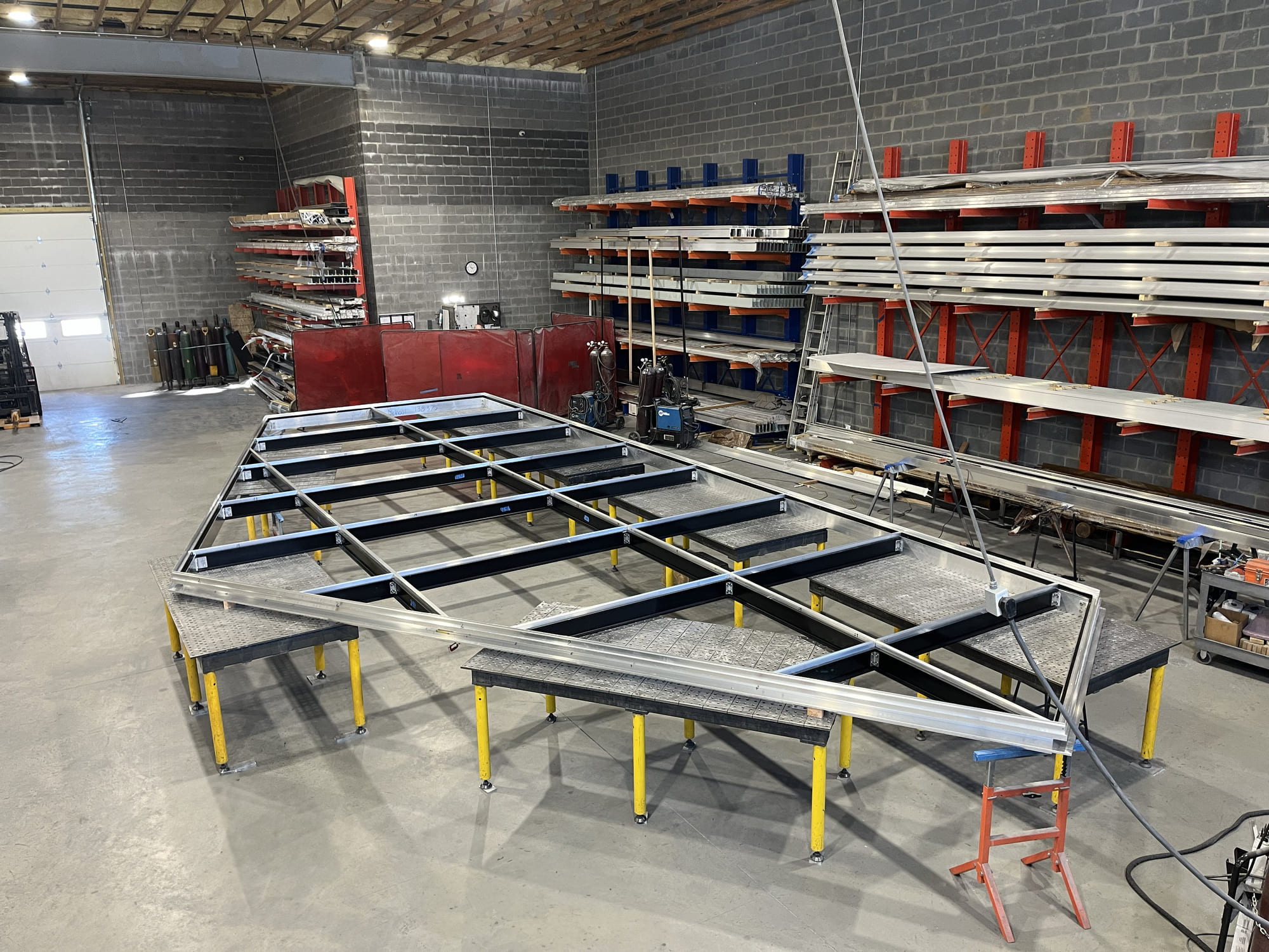 Industrial glass workshop with large metal frames and glass panels prepared for fabrication.