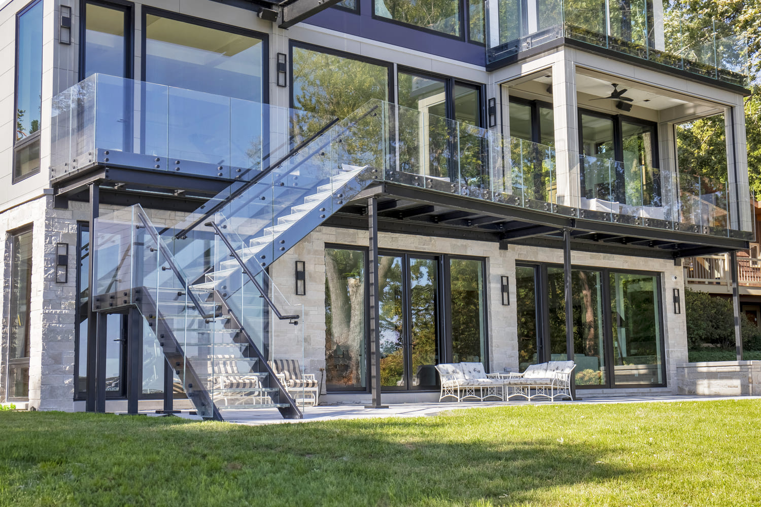 Backyard view of a modern home with glass staircases leading to upper levels.