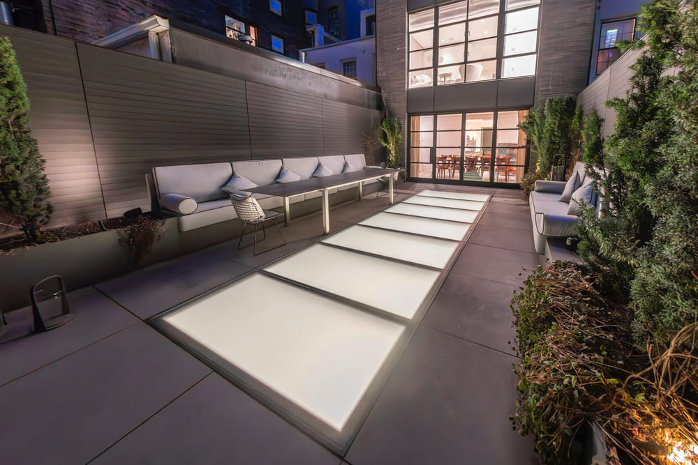 A modern rooftop lounge featuring long illuminated glass floor panels and seating areas.