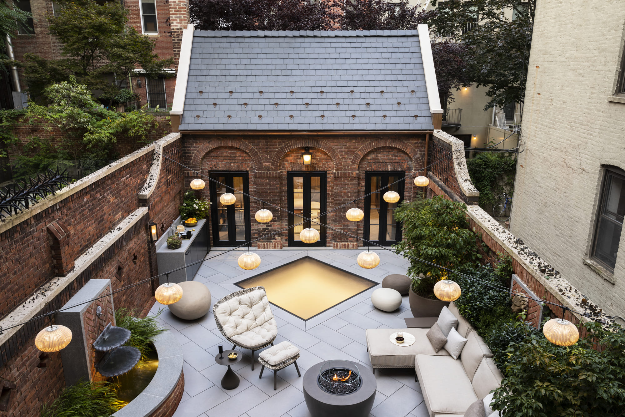 Urban rooftop patio surrounded by greenery, featuring a central skylight and outdoor seating.