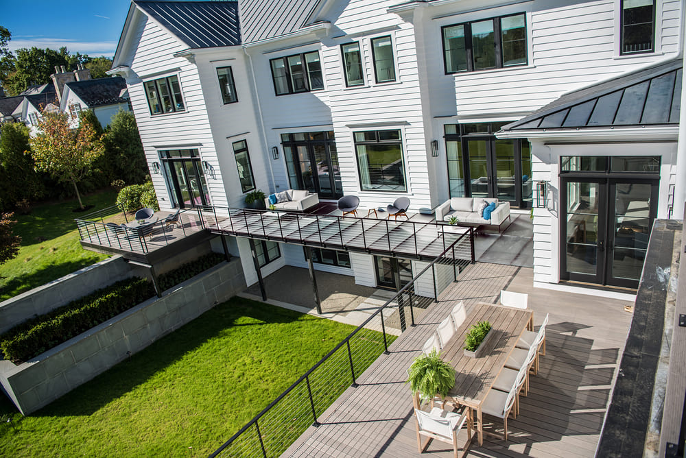 Tempered glass sheets installed as exterior deck flooring on a modern white home with outdoor seating.