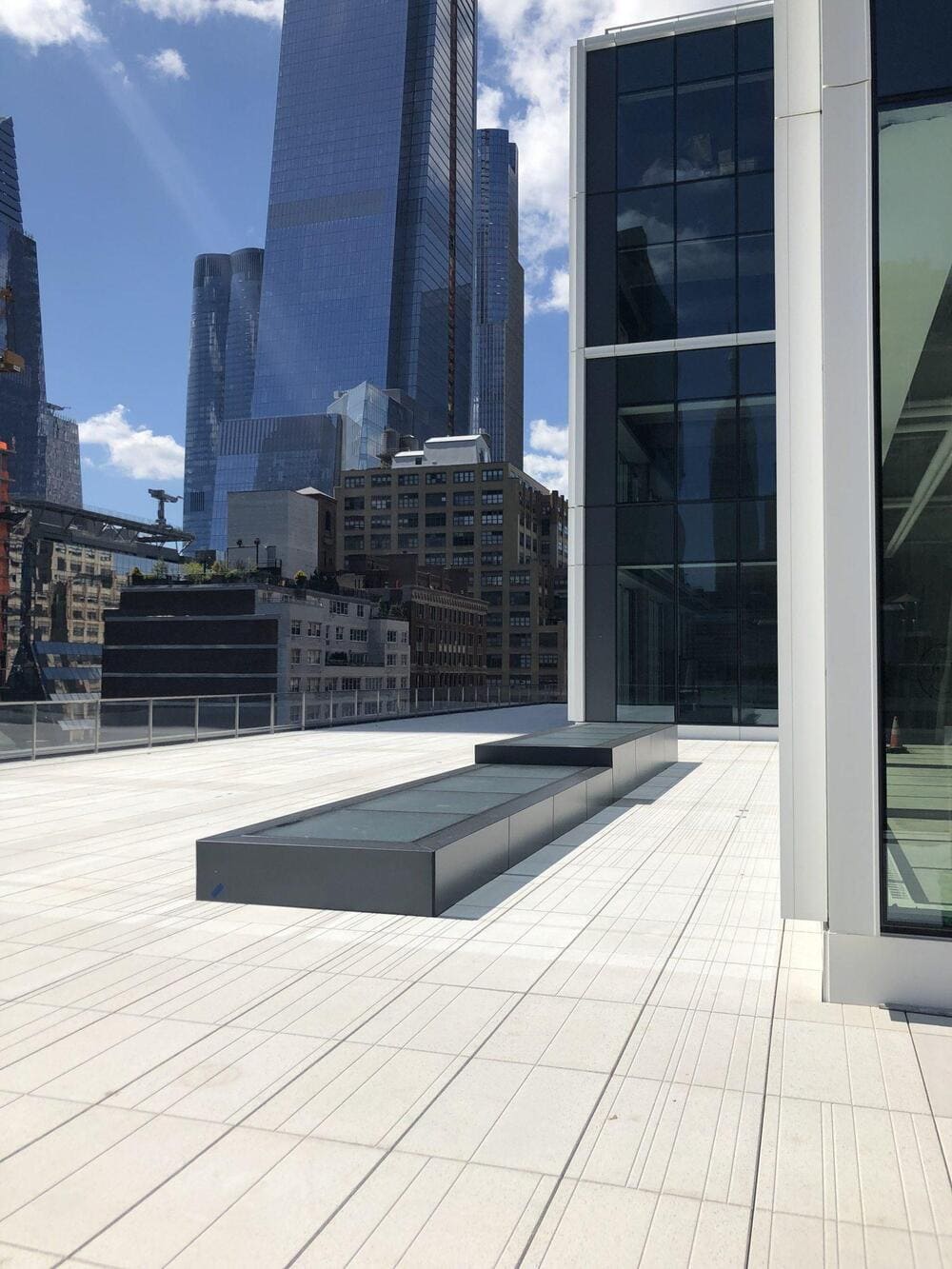 A modern rooftop patio with glass floor panels overlooking a city skyline.