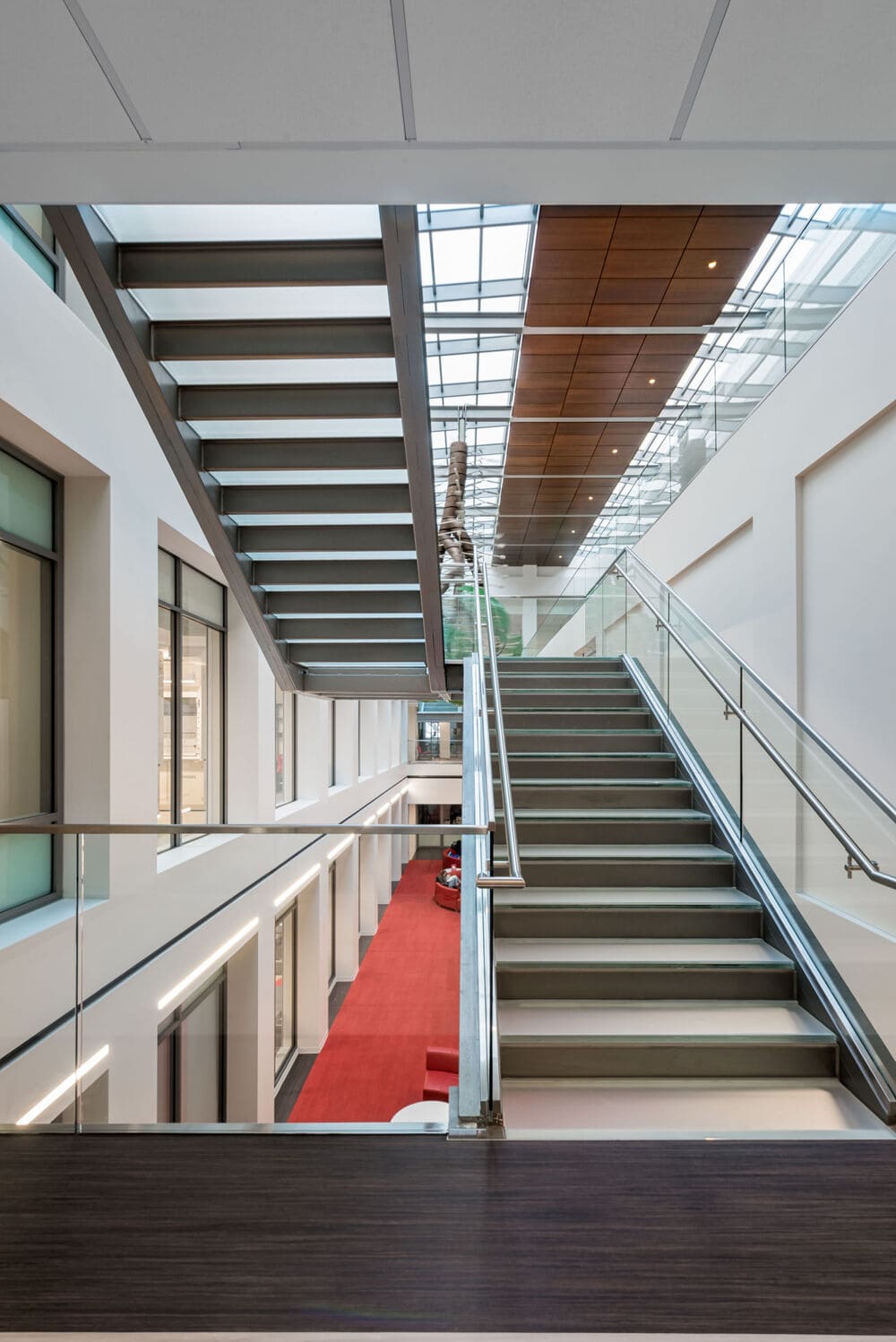 Indoor glass staircase with transparent railings and a view of the ceiling skylight.
